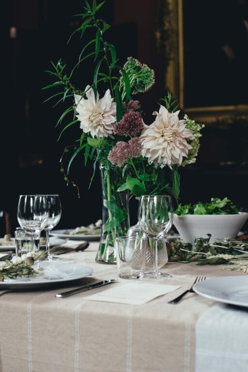 Elegant dining table set with white plates, glassware, and a vibrant floral centerpiece in a dimly lit room.